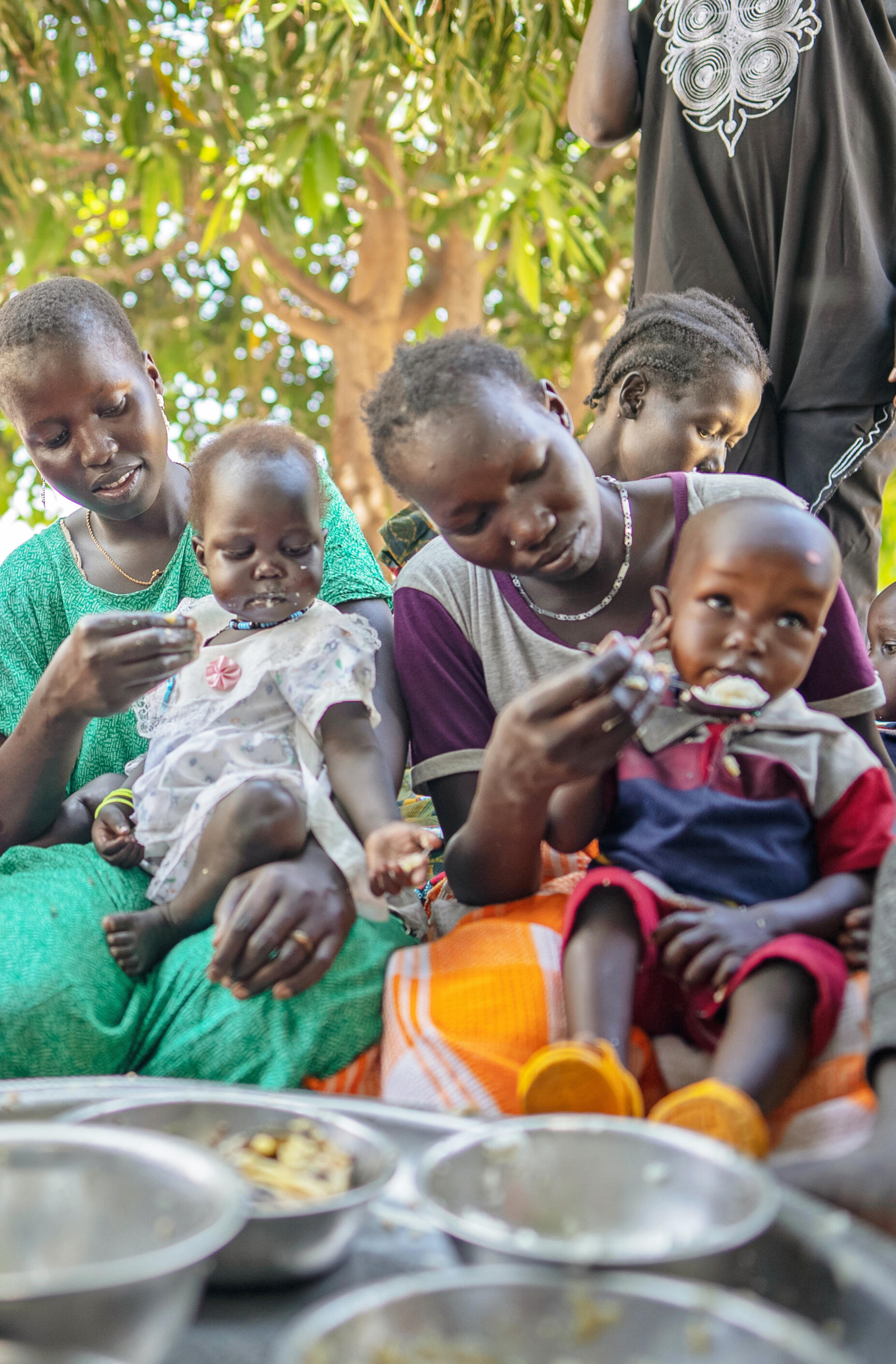 © UNICEF/UNI438985/ On 28th February 2023, Tapitha Nyakhan Gatwich (in green), head of a UNICEF-supported mother to mother support group, is photographed eating with other mothers at Bieh IDP camp in Bentiu, Unity State, South Sudan.